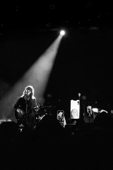 Gracie Abrams under a single spotlight while phone screens glow in the dark crowd