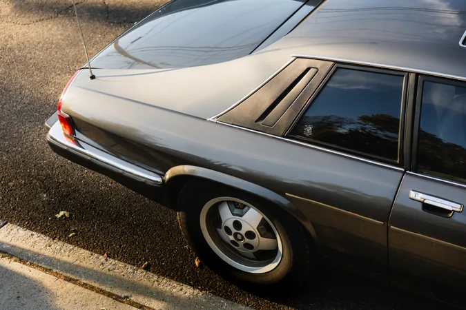 The rear haunch and louvred quarter window of a grey coupe parked at the kerb