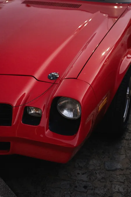 The front fender and round headlight of a red 1970s muscle car