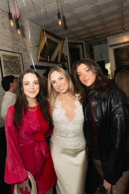 Three guests posing together at a party under warm hanging lights