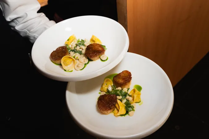Two plates of seared scallops carried to the table