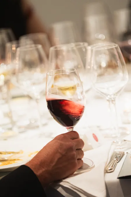Guest holding a glass of red wine at a candlelit dinner