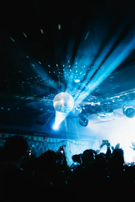 A mirror ball scattering blue beams over a crowd of raised hands and phones