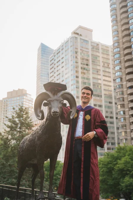 Law graduate in cap and gown beside the Fordham ram statue