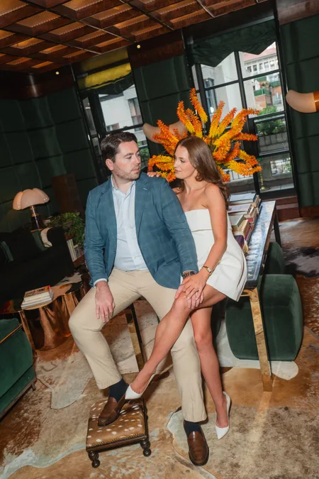Ned and Alison posed together in a green velvet New York City lounge beneath an orange floral arrangement