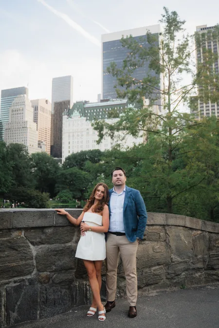 Ned and Alison on a stone bridge in Central Park with the Midtown Manhattan skyline behind them