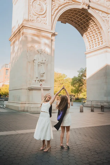 Graduate and friend cheering under the Washington Square Arch