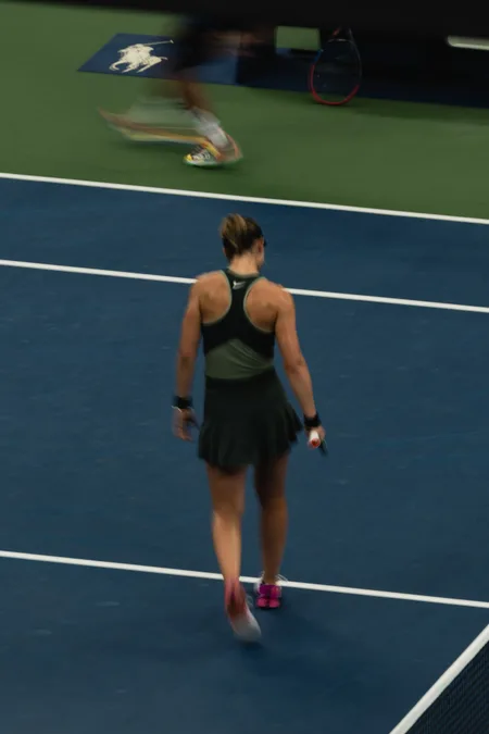 A player walking the baseline while an opponent blurs past behind