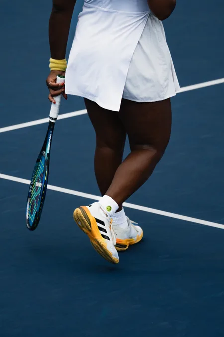 A player in white stepping across the baseline, racket held low