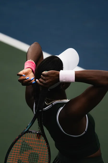 A player tying her hair back behind a white visor between points