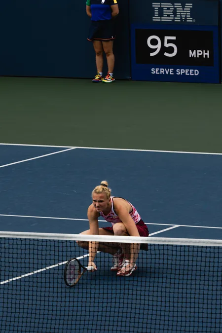 Kateřina Siniaková crouching at the net beneath a board reading 95 miles per hour