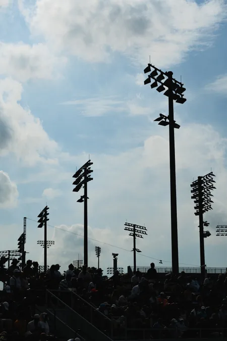 Floodlight towers rising over the stands under a bright cloudy sky