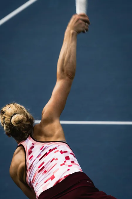 Kateřina Siniaková serving, seen from behind with her racket arm fully extended