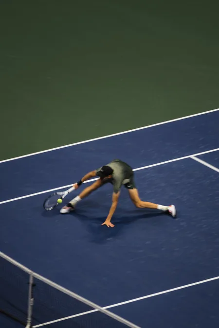 A player stretching low to dig out a ball under the lights