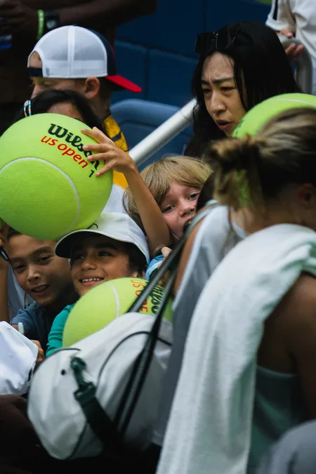 Young fans crowding the rail with oversized US Open balls