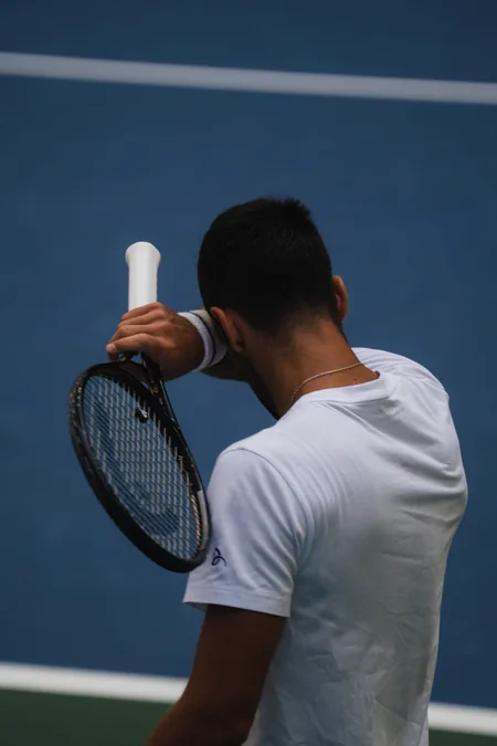 A player pressing a forearm to his face, racket raised beside him